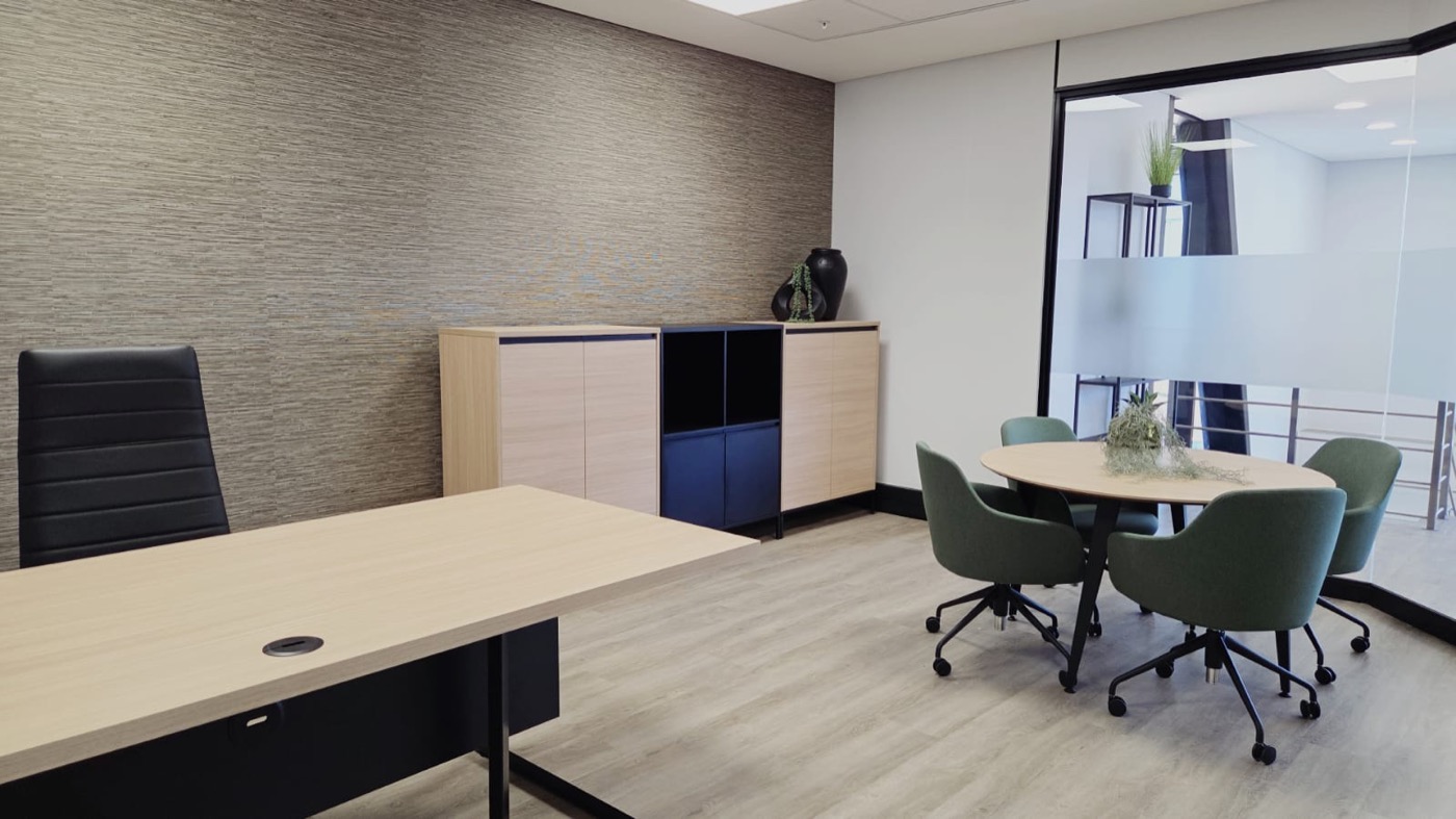Completed executive office with textured wall treatment, pale timber desk, storage, and green meeting chairs