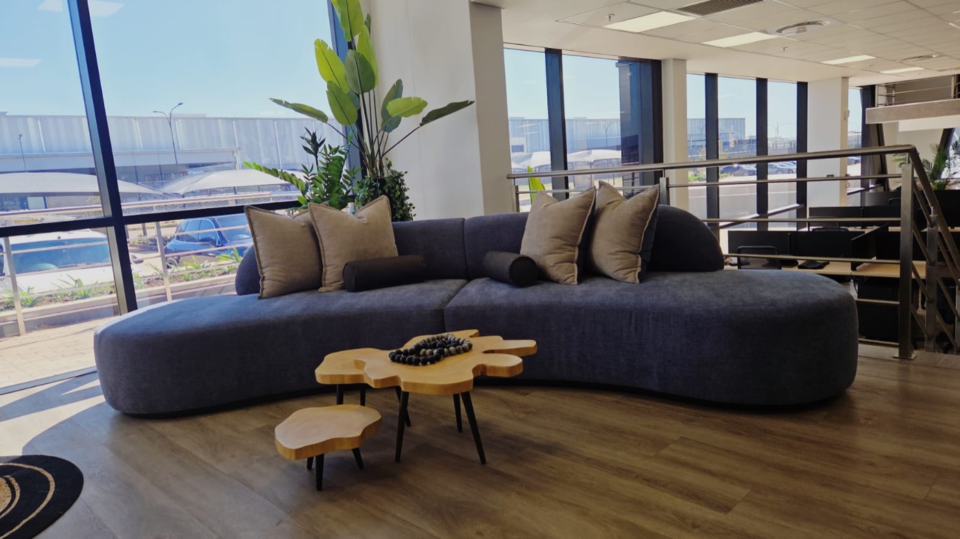 Completed lounge seating detail with curved sofa, layered cushions, timber tables, and indoor greenery