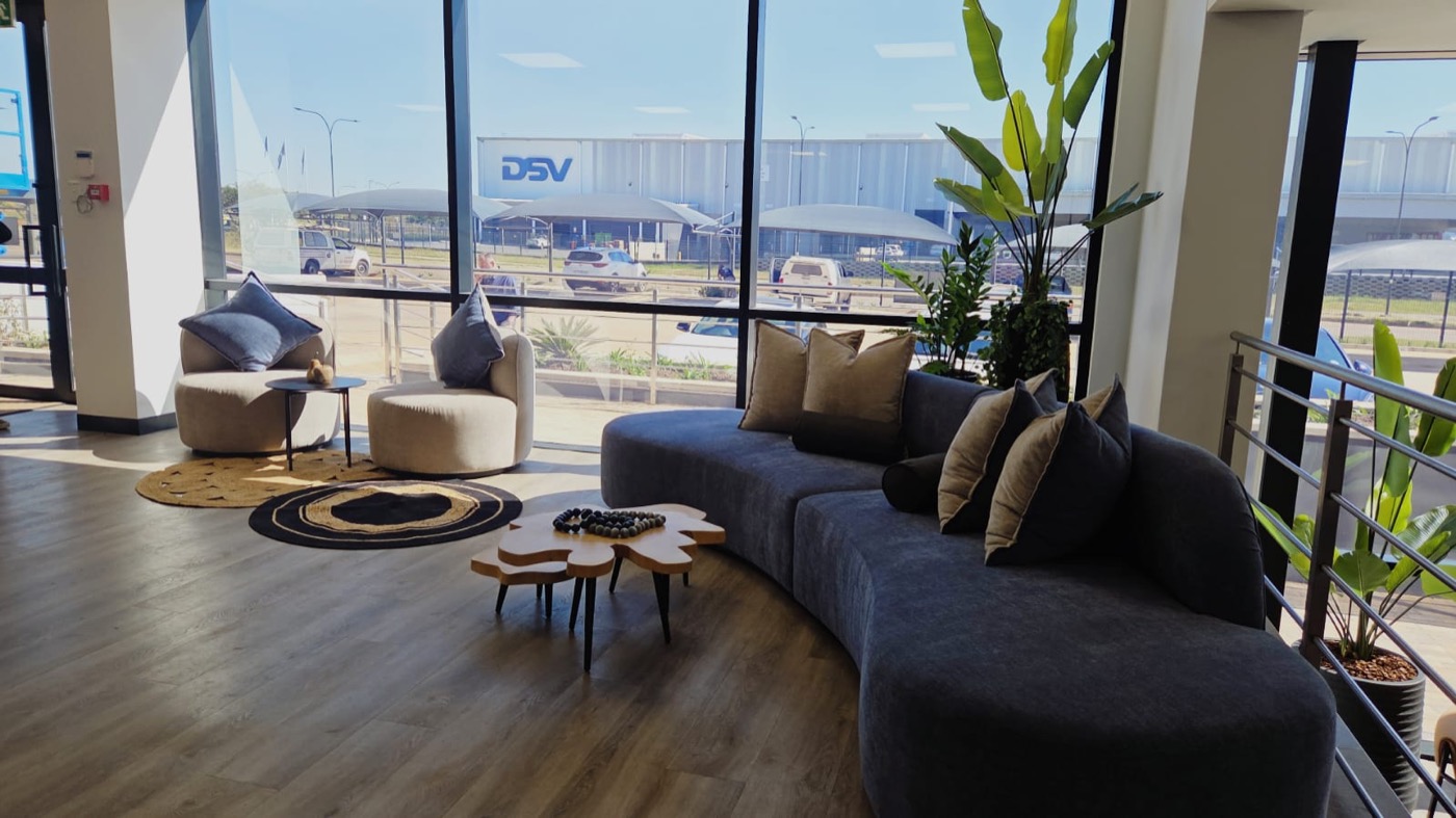 Completed Arialex reception lounge with curved sofa, timber tables, greenery, and layered rugs